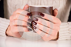 Girl with brown nails manicure holds cup of coffee on desk