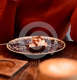 A girl in a brown sweater in a cafe eats a piece of cake on a plate with a fork. focus on cake. breakfast, start of a new day