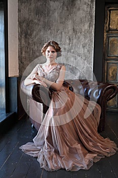 The girl the brunette in a beautiful dress poses opposite to a window