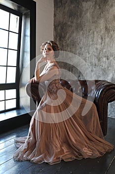 The girl the brunette in a beautiful dress poses opposite to a window