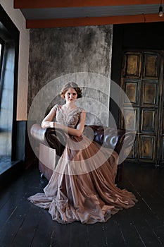 The girl the brunette in a beautiful dress poses opposite to a window