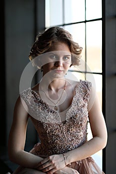 The girl the brunette in a beautiful dress poses opposite to a window