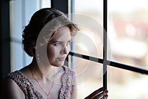 The girl the brunette in a beautiful dress poses opposite to a window