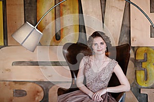 The girl the brunette in a beautiful dress poses sitting in a seat against the background of the wall issued in the abstract style