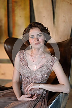 The girl the brunette in a beautiful dress poses sitting in a seat against the background of the wall issued in the abstract style