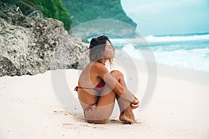 Girl Brunette with curly hair in a red bikini on the beach with white sand near the ocean on vacation. A beautiful model