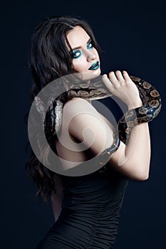 girl brunette green make up eyes gaze close up portrait with a snake yellow brown mottled python on a blue background