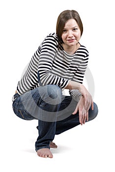 Girl brunette sitting barefoot in a striped shirt and blue jeans.