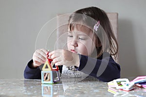 A girl is building a toy house sitting at a table