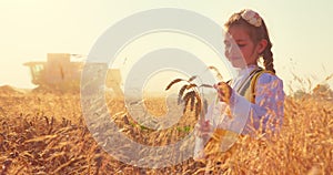 Girl with Bulgarian folklore costume at the agricultural wheat field during harvest time with industrial combine machine