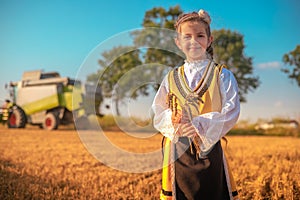 Girl with Bulgarian folklore costume at wheat field during harvest with combine by sunset