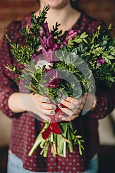 A girl in a burgundy blouse holds a bouquet of tulips, boxwood and plants with a manicure