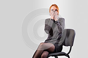 A girl, in business clothes, covers her face with her hands in fright, on a gray background