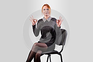 A girl in a business suit shows an okay sign, on a gray background.