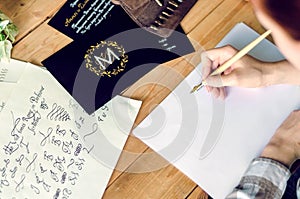 A girl calligrapher paints pen on white paper behind her working wooden table.