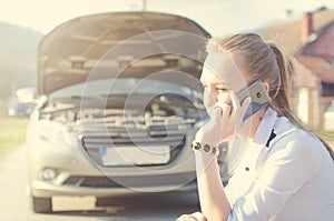 Girl calling. Broken car on a background. Woman sit on a wheel. young woman repair a car. Natural background. Car accide