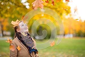 Girl in a camel coat in autumn park smiles and catches falling leaves