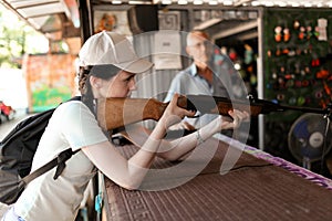 A girl in a cap and with a backpack took a rifle in her hands and aims at a target in a shooting gallery