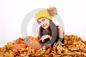 Girl in cap with bobbles lying on autumn leaves by pumpkins