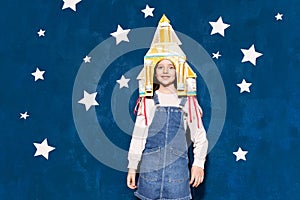 Girl with cardboard rocket posing on studio background with paper stars.