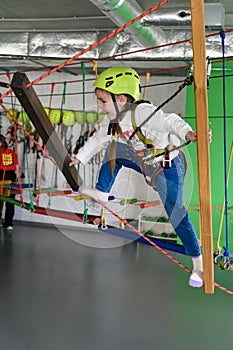 The girl carefully and cautiously passes the cableway in the playroom.