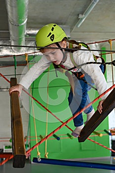 The girl carefully and cautiously passes the cableway in the playroom.