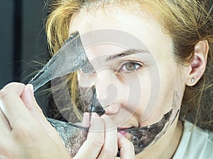 The girl carefully removes from her face a black thin transparent mask for cleaning pores