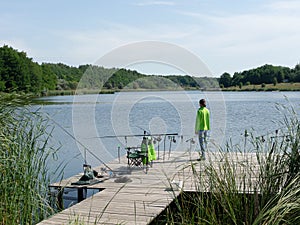 Girl carp fishing on beautiful blue lake with carp rods and rod pods in the summer morning. Fishing from the wooden