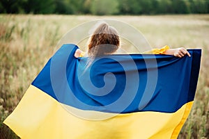 Girl carries fluttering blue and yellow flag of Ukraine in field.