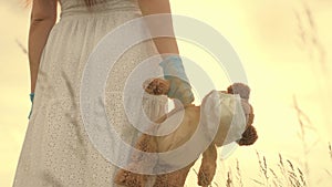 A girl carries in her hand toy teddy bear with medical mask in summer park. child holds his beloved teddy bear in