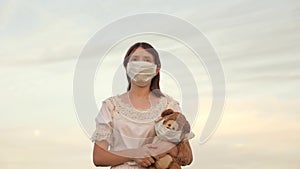 A girl carries in her hand toy teddy bear with medical mask in summer park. Covid-19 pandemic coronavirus. Child health