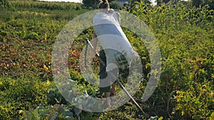 The girl is carrying a bag of grass and a scythe around the garden. Beautiful landscape. Work in the field. Real rural