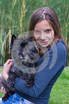 Girl carrying black dog on arm in nature