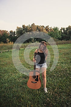 A girl carrying a guitar on a meadow