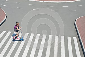 Girl carrying scooter and crossing road on way to school. Zebra traffic walk way in the city. Pedestrian passing a crosswalk.