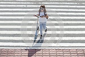 Girl carrying scooter and crossing road on way to school. Zebra traffic walk way in the city. Pedestrian passing a crosswalk.