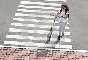 Girl carrying scooter and crossing road on way to school. Zebra traffic walk way in the city. Pedestrian passing a crosswalk.