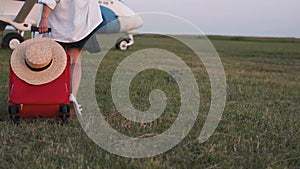 A girl is carrying a suitcase to the plane across the field close-up. Travel suitcase on wheels in hand and female legs