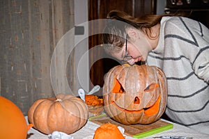 A girl carving big orange pumpkin into jack-o-lantern for Halloween holiday decoration at kitchen. Decoration for party