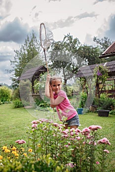 Girl catches butterfly in village garden at summer, young bug-hunter, happy vacation in countryside