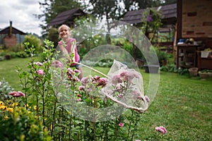 Girl catches butterfly in village garden at summer, young bug-hunter, happy vacation in countryside