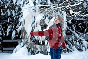 A girl of Caucasian appearance in a burgundy sweater throws snow. Outdoor games. Winter day, snowy park