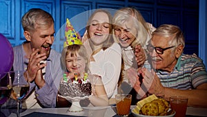 Girl celebrating birthday party with parents, senior grandparents family blowing out candles on cake