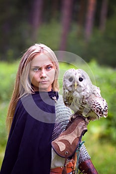 Girl in chain mail holding owl in forest