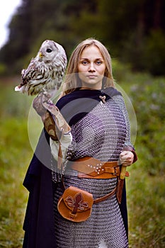 Girl in chain mail holding owl in forest