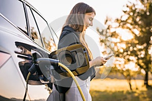 Girl charging electric car and adjusting an EV charging app on smartphone