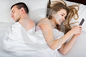Girl chatting with mobile, man sleeping by in bed