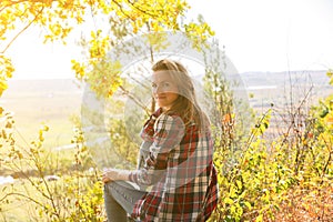 Girl in the checkered shirt is sitting in the autumn forest. Seasonal concept. Stylish hipster clothes outdoors. Nature philosophy