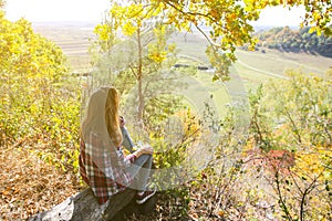 Girl in the checkered shirt is sitting in the autumn forest. Seasonal concept. Stylish hipster clothes outdoors. Nature philosophy