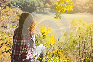 Girl in the checkered shirt is sitting in the autumn forest. Seasonal concept. Stylish hipster clothes outdoors. Nature philosophy